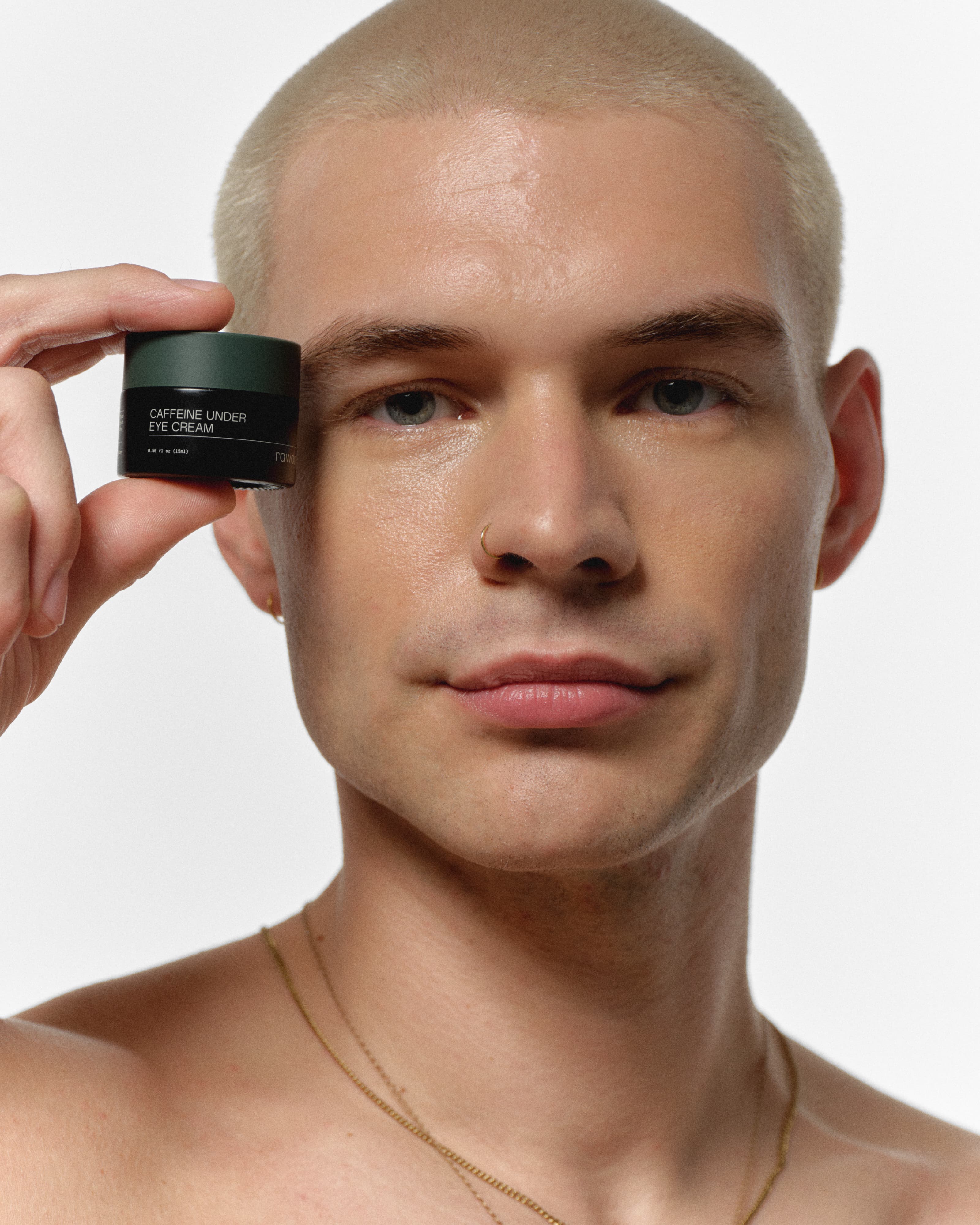 Model holding RAWDOG Caffeine Under Eye Cream beside his eye