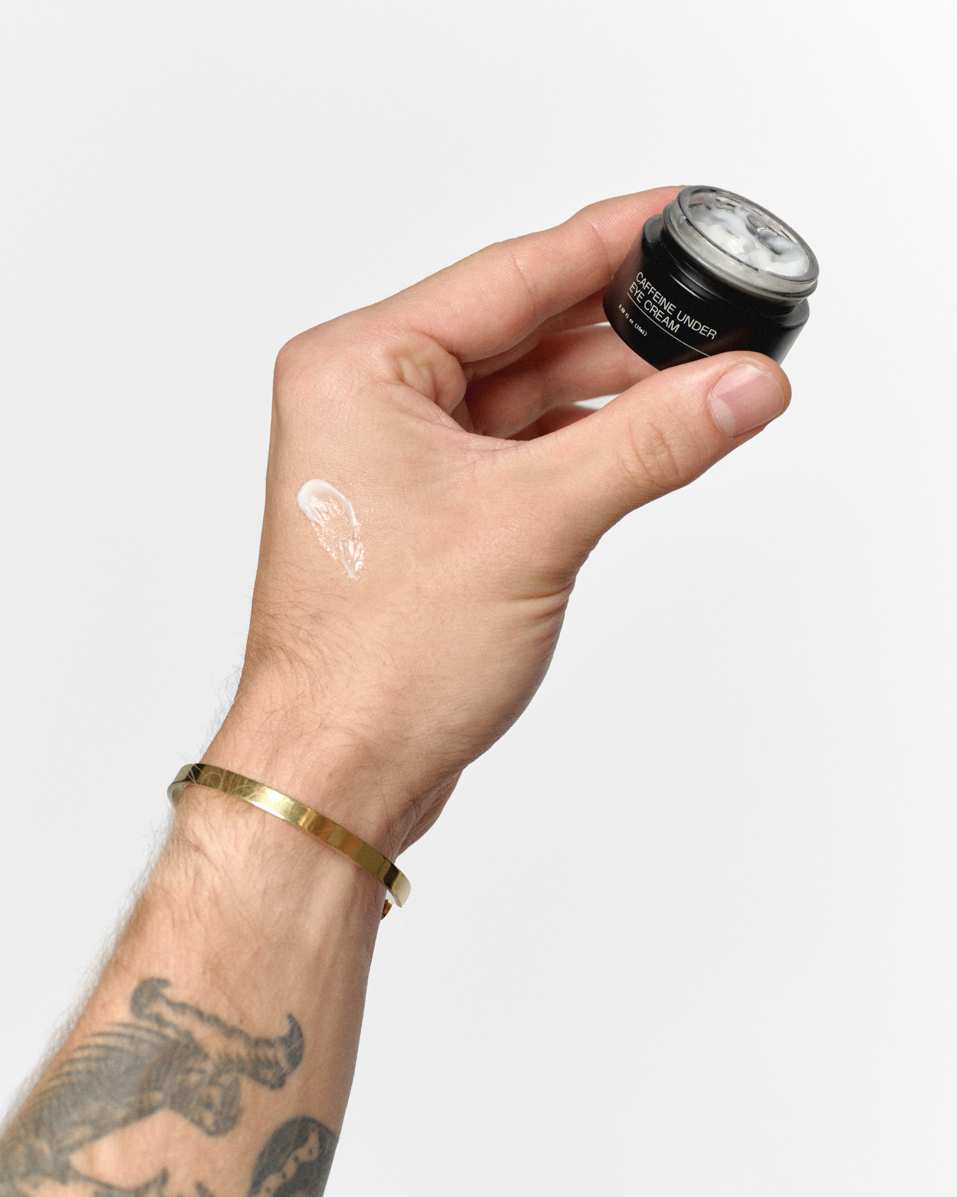 Hand holding open RAWDOG Caffeine Under Eye Cream with product texture swatch