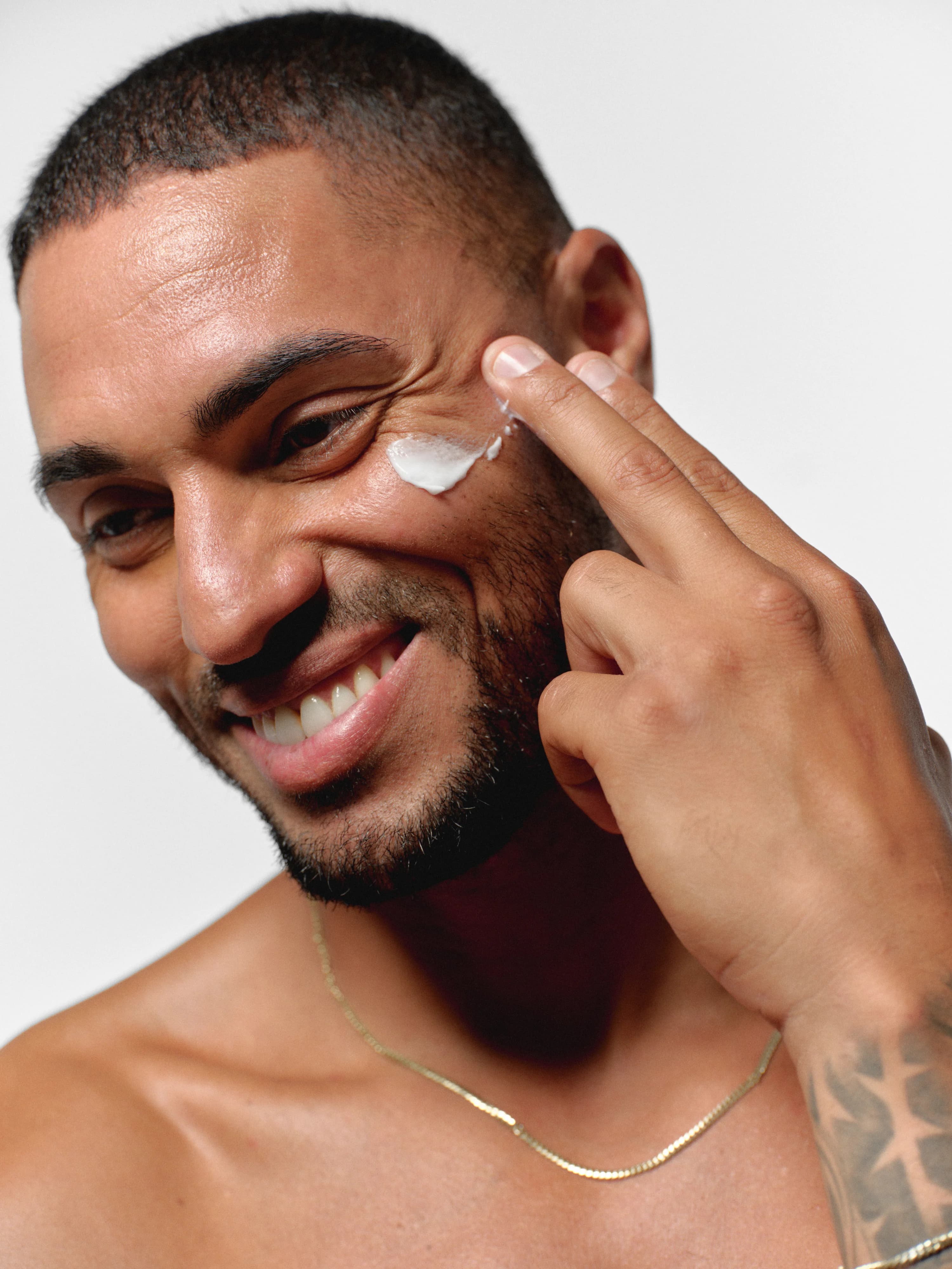 Man smiling while applying RAWDOG face moisturizer to his cheek